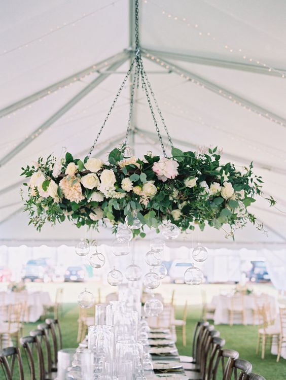 a long table is set up under a tent with flowers and candles hanging from the ceiling