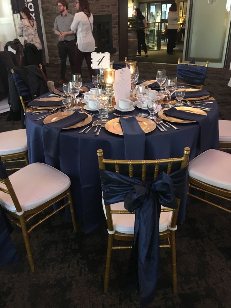 a table set up with blue cloths and gold place settings for an elegant dinner