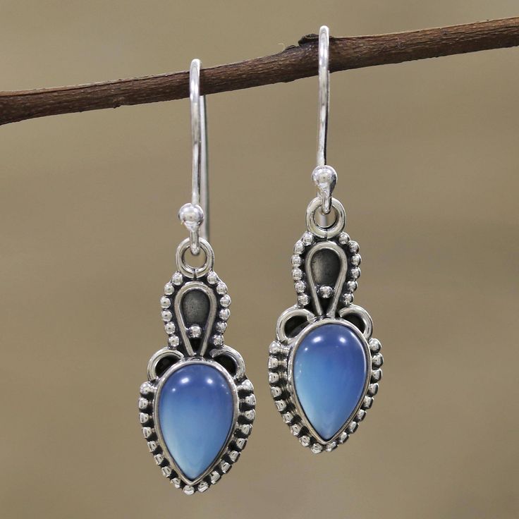 Considered by some to absorb negative energy, cool blue chalcedony is intriguing in these earrings from Alok Jain. Artisans set the cabochon gems in sterling silver bezels and surround them with silver rawa or granules. Contrasting oxidization adds interest to the unique earring design. The earrings swing from sterling silver hooks. Chalcedony Drop Earrings As Gift, Drop Chalcedony Earrings As A Gift, Chalcedony Dangle Jewelry With Matching Earrings, Blue Moonstone Earrings For Gift, Chalcedony Dangle Earrings With Matching Jewelry, Blue Chalcedony Dangle Jewelry, Blue Moonstone Drop Earrings, Blue Drop Jewelry With Cabochon, Blue Cabochon Drop Jewelry