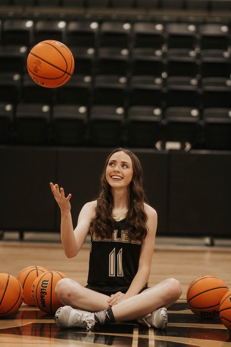 a woman sitting on the floor with basketballs in front of her and looking up