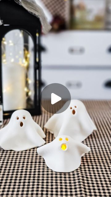 two white ghost figurines sitting on top of a table next to a lantern