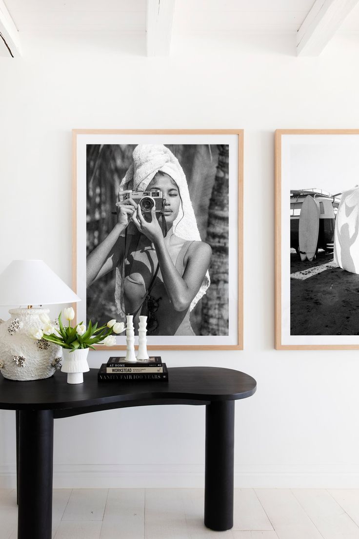 two black and white photos hang on the wall next to a table with vases