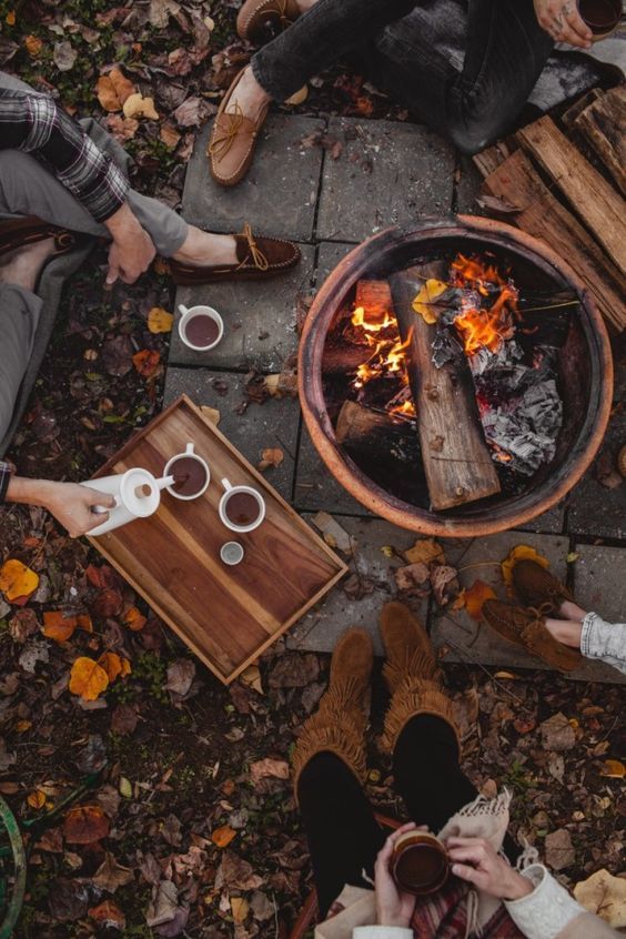 three people sitting around a fire pit with coffee and marshmallows on the ground