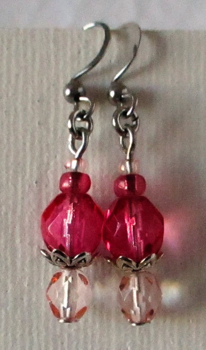 two red glass beads are hanging from silver earwires on a white fabric background