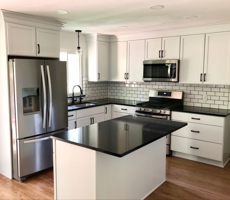 a kitchen with white cabinets and black counter tops, stainless steel appliances and an island in the middle