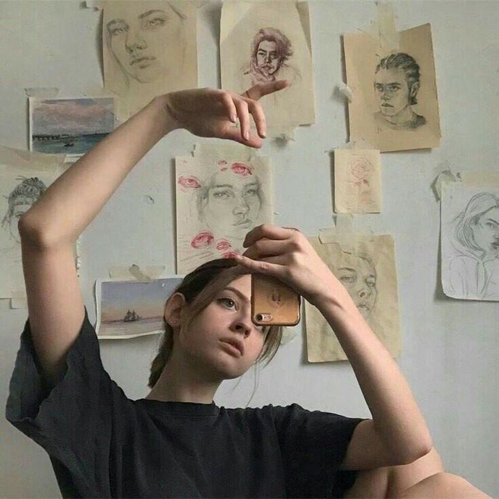 a woman holding her head in front of a wall with drawings and pictures on it