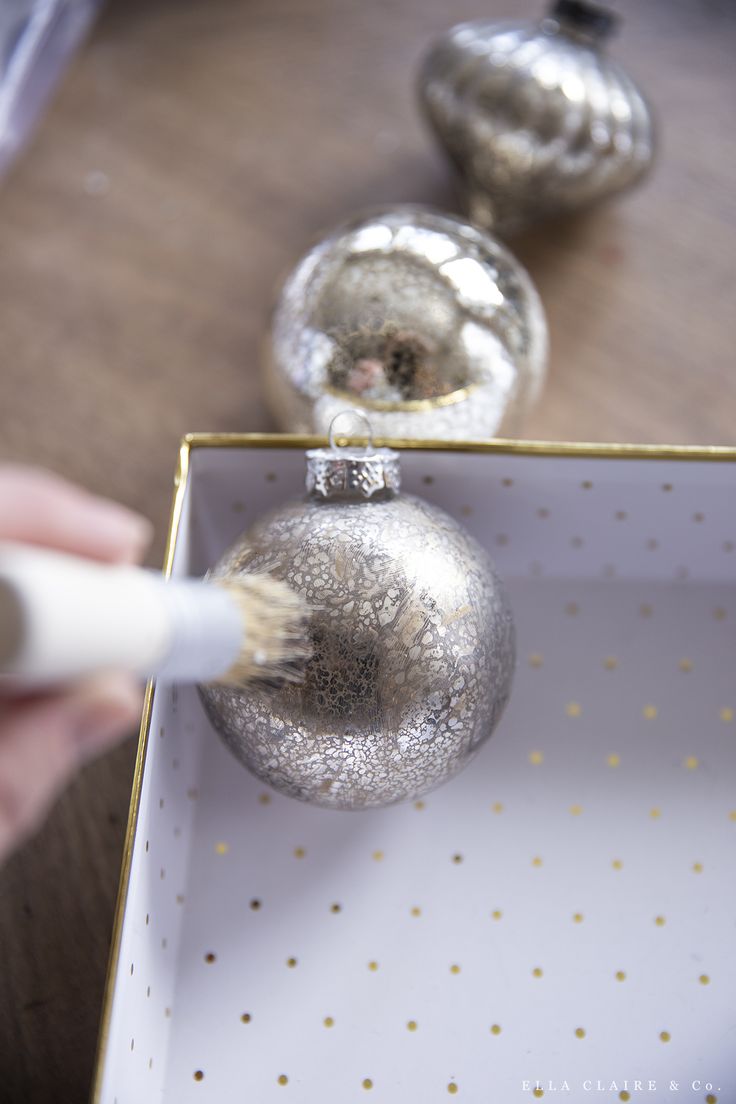 a person is painting a silver ornament on a white box with gold dots