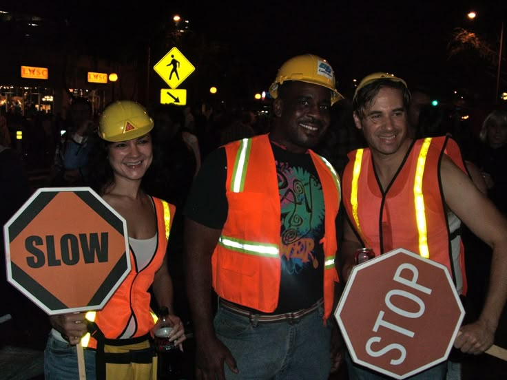 three people wearing safety vests and holding stop signs in front of a crowd at night