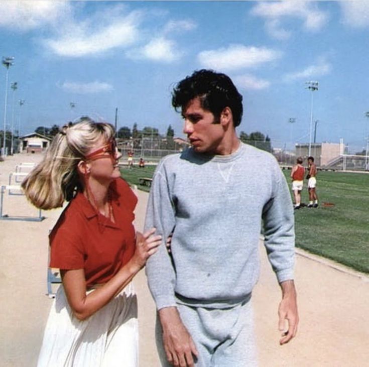 a man and woman walking on a baseball field with the sky in the back ground