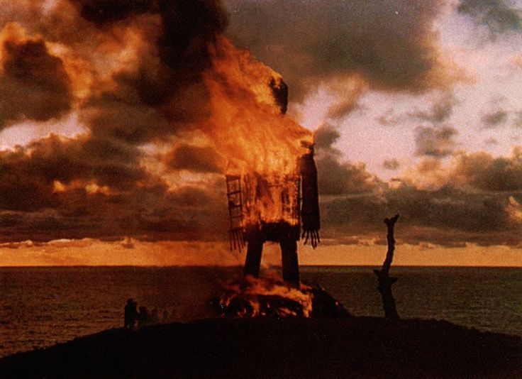 a giant fire hydrant on top of a hill next to the ocean with people standing around it