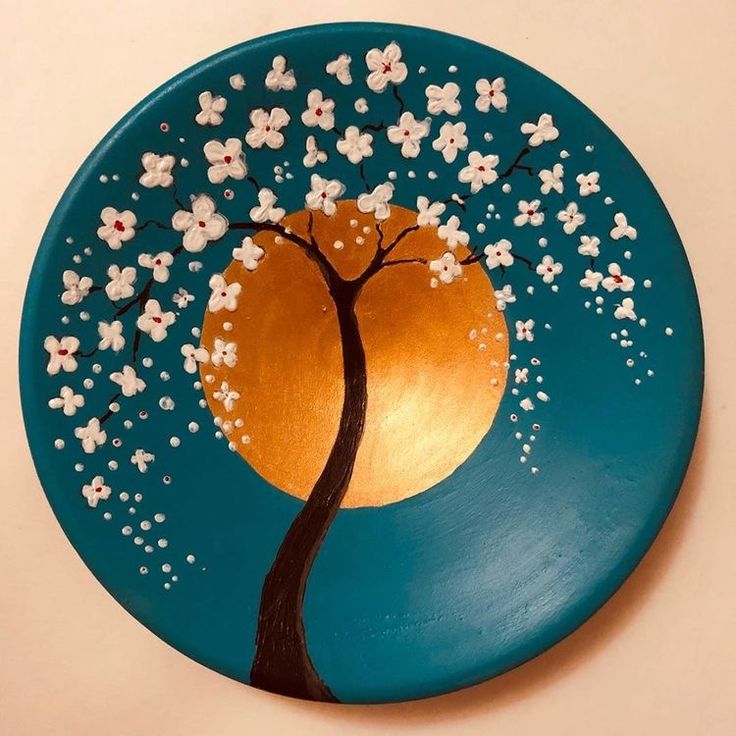 a blue plate with white flowers and a tree painted on the front in gold, silver and teal