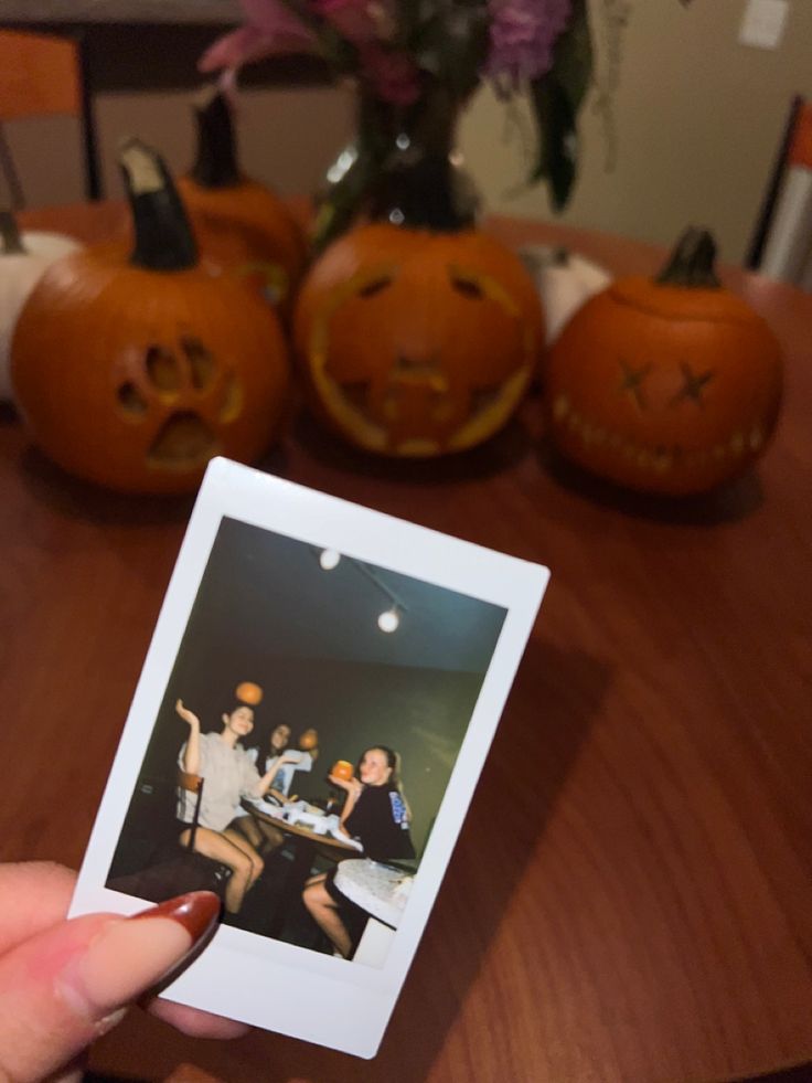 a person holding up a polaroid with halloween pumpkins in the background on a table