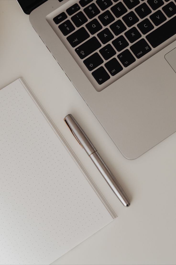 an open laptop computer sitting on top of a desk next to a pen and paper