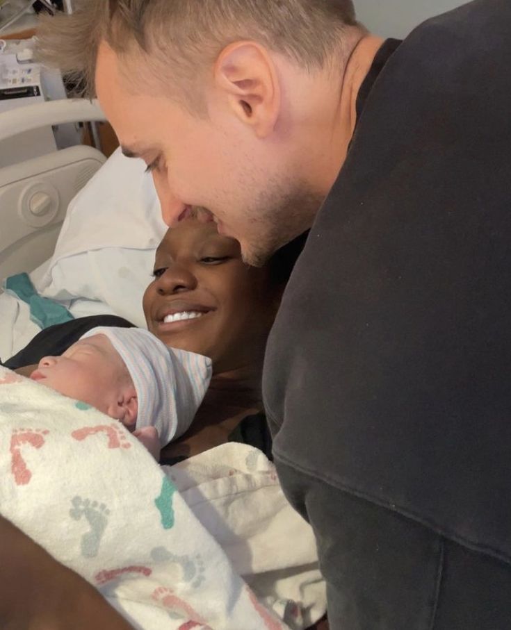 a man holding a baby in his arms and smiling at the camera while he lays down next to him