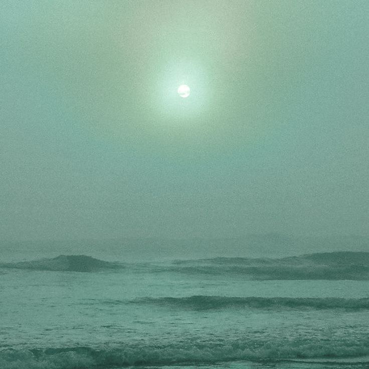 the sun is shining over the ocean on a foggy day