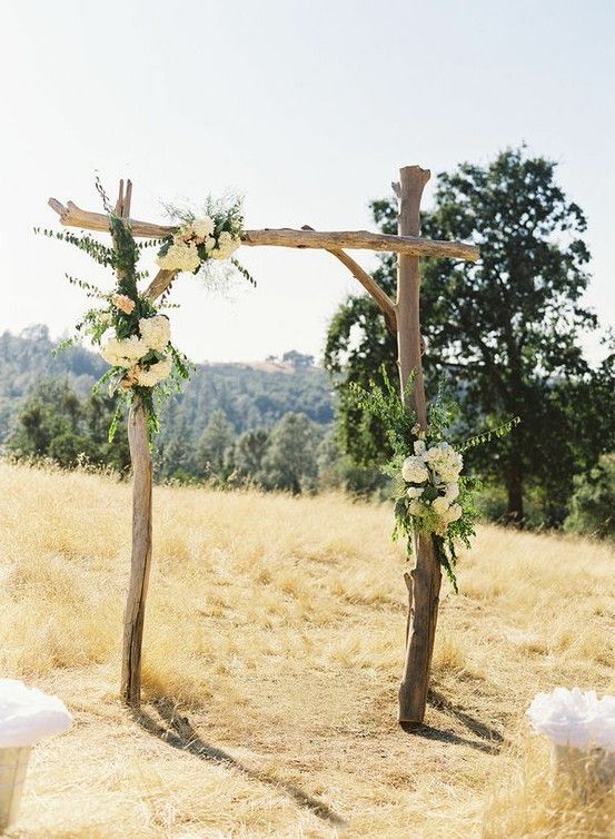 a wooden cross with flowers on it in the middle of an open field, surrounded by grass