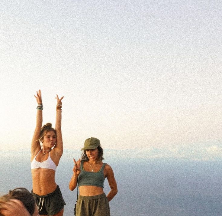 two women standing on top of a mountain with their arms in the air and one holding her hands up