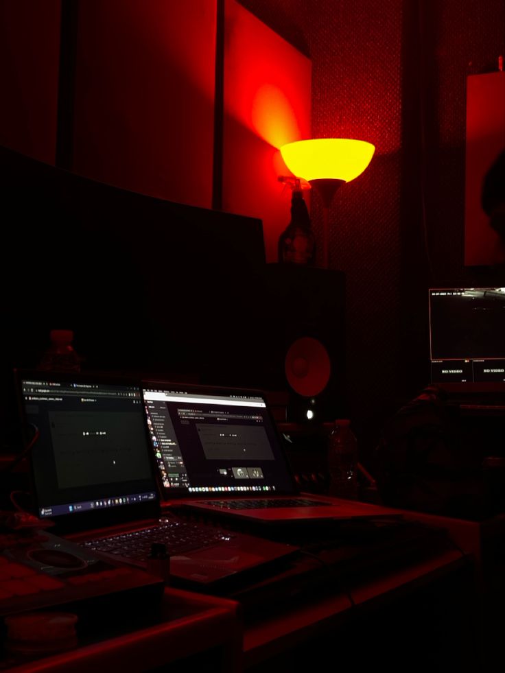 two laptops are sitting on a desk in the dark with red light coming from behind them