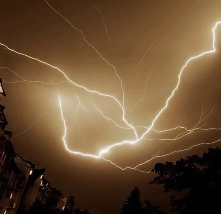 lightning strikes in the night sky over a building and street lights on a dark cloudy day