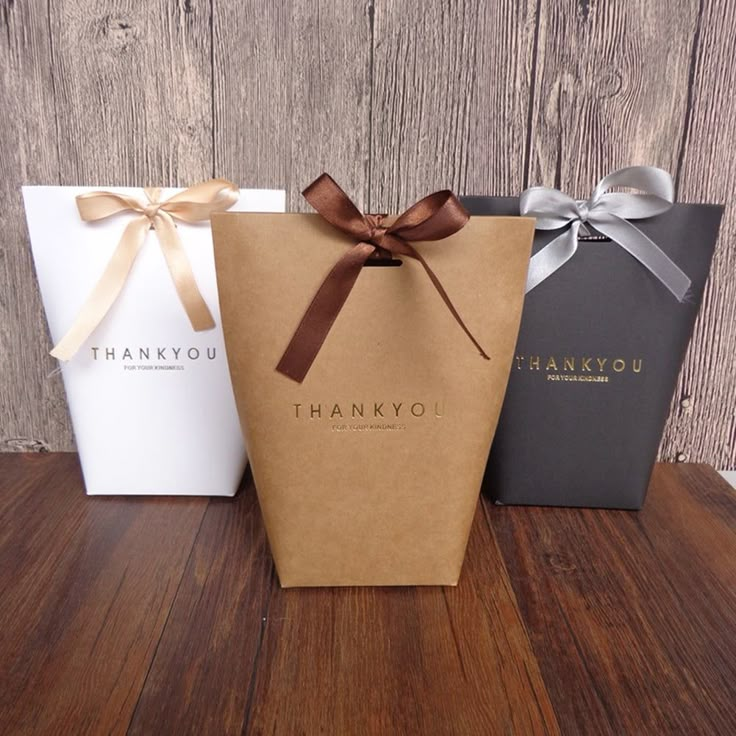 three thank you bags with brown bows on them sitting on top of a wooden table