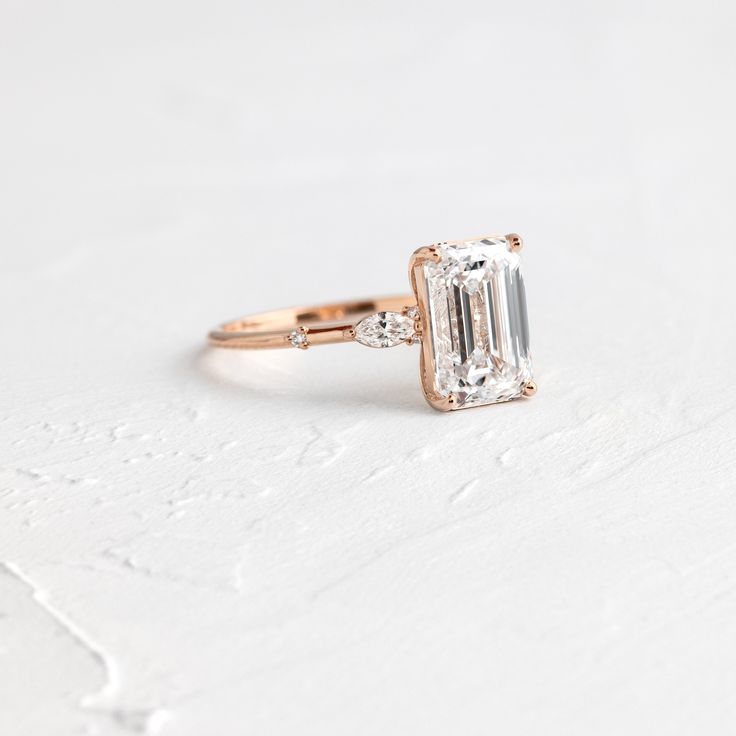 an emerald cut diamond engagement ring with two side stones on the band, set in 18k rose gold