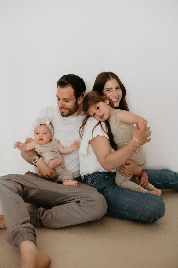 a man and woman sitting on the floor with two babys in their arms, smiling at the camera