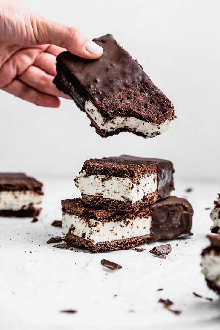 someone is picking up an ice cream sandwich from the table with chocolate and marshmallows on it