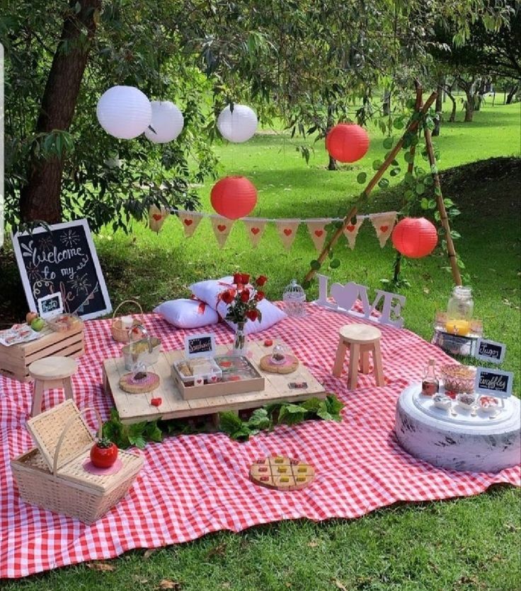 an outdoor picnic is set up with red and white balloons, food and drinks on a checkered tablecloth