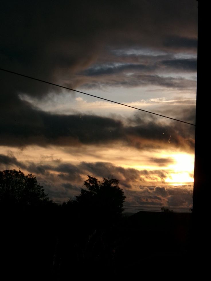 the sun is setting behind dark clouds in the sky above some trees and power lines