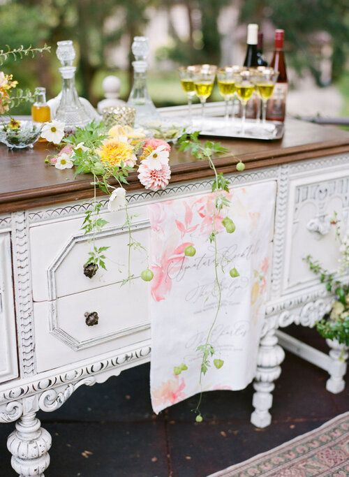 an old dresser with flowers on it and wine glasses sitting on top of the drawers