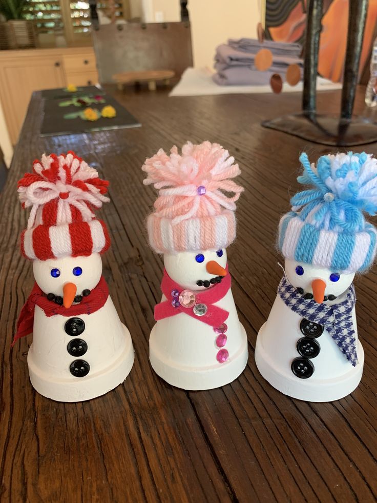 three snowmen with hats and scarves are sitting on a wooden table in front of a fireplace