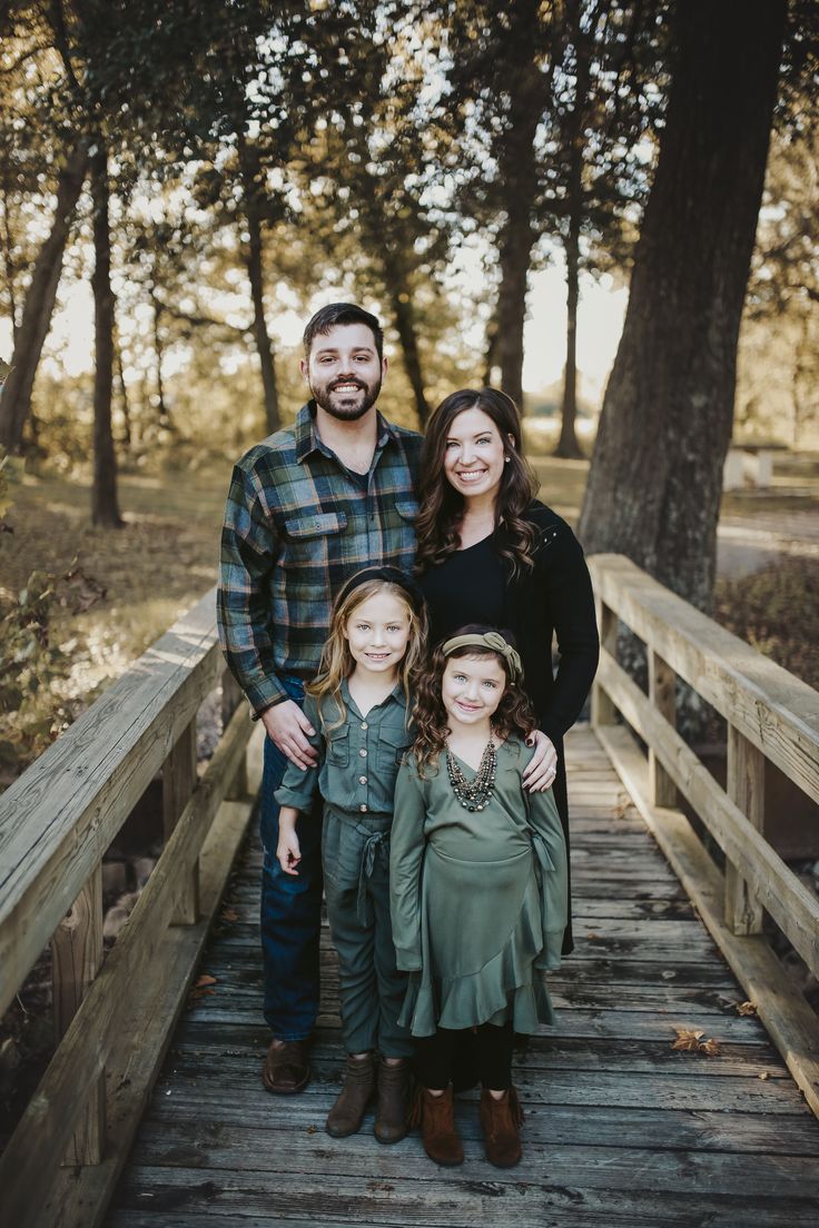 a family poses on a bridge in the woods for an outdoor photo session at sunset