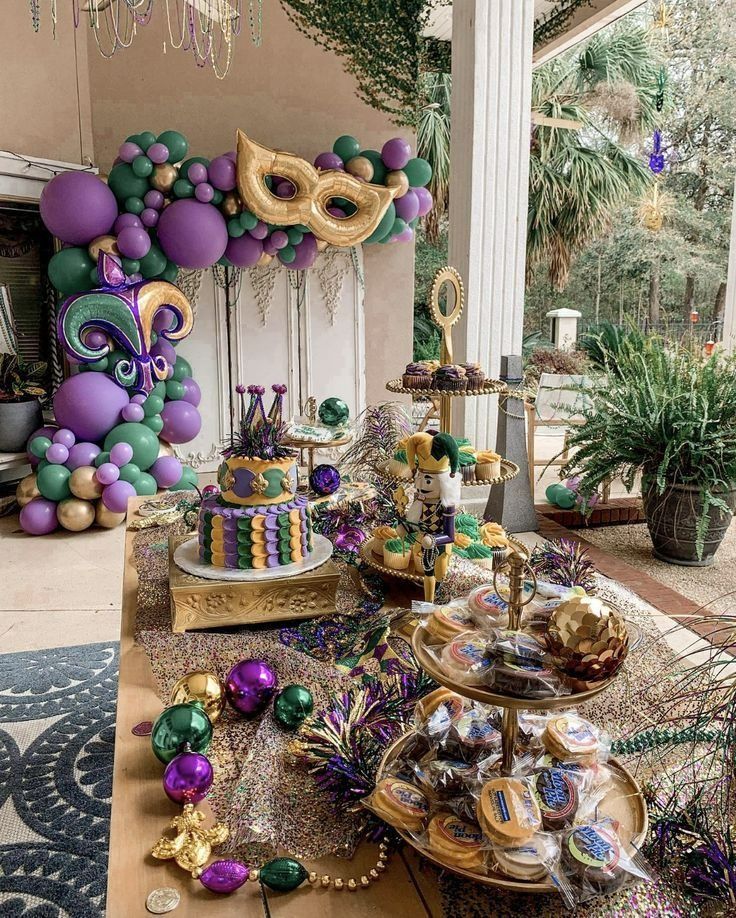 a table topped with lots of cakes and desserts covered in purple, green and gold balloons