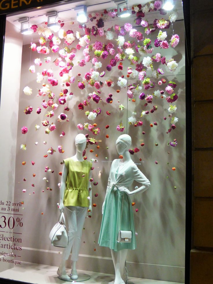 two mannequins in front of a display window with flowers on the wall