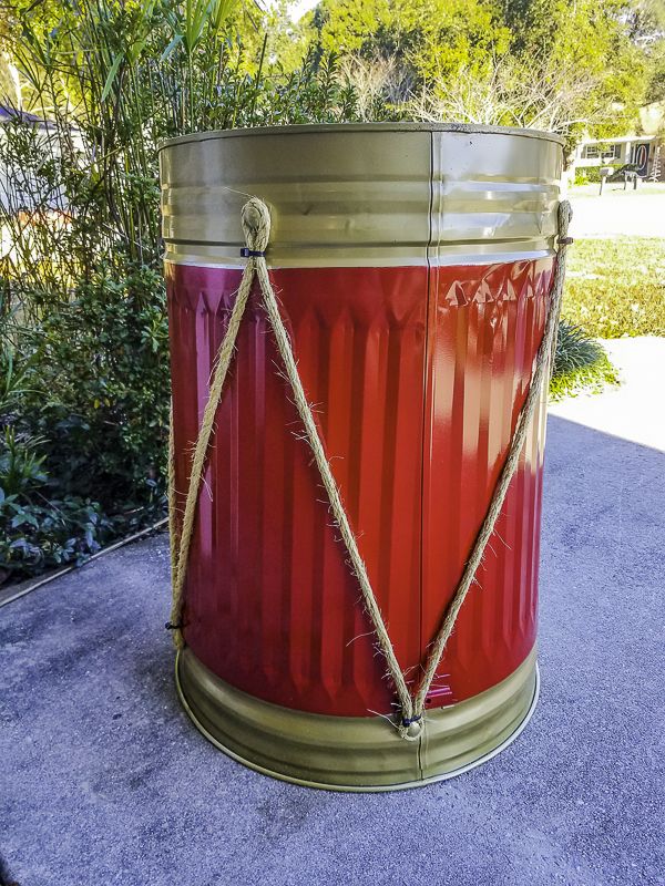 a red and gold trash can with rope wrapped around the top, sitting on concrete