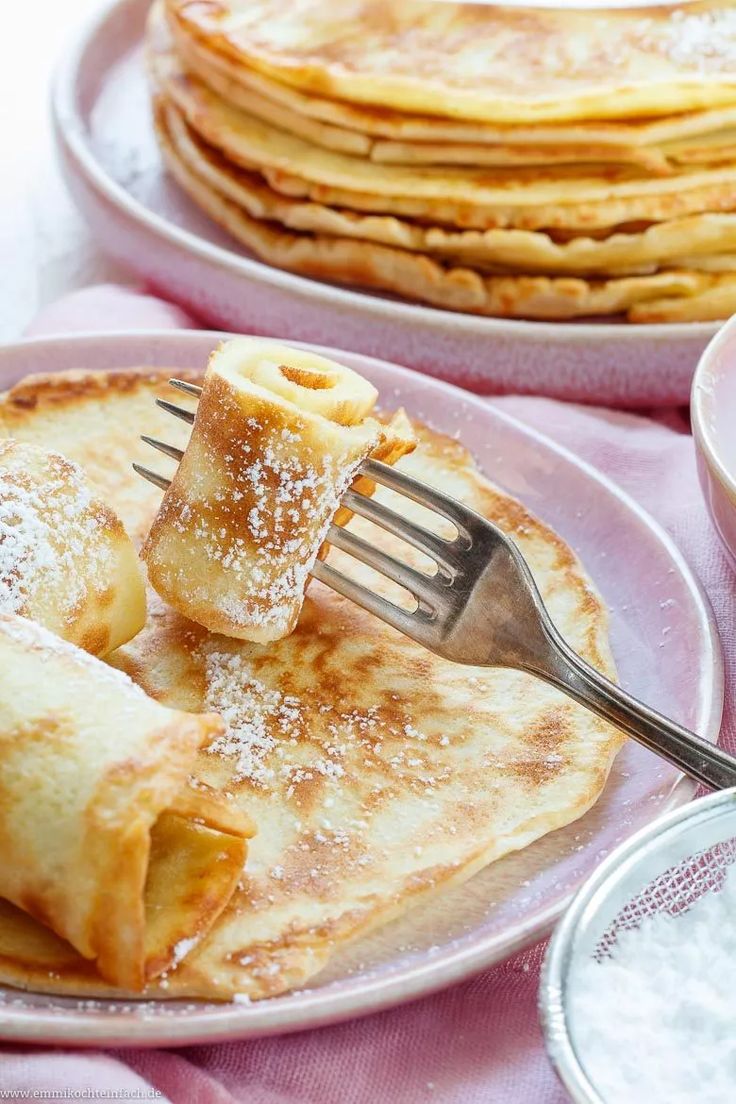 pancakes with powdered sugar on them and a fork in the middle, ready to be eaten