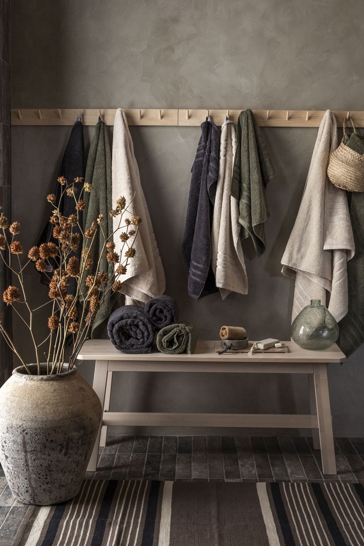 a bench with towels hanging on it next to a vase filled with flowers and plants