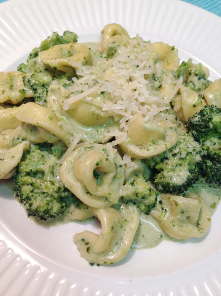 a white plate topped with pasta and broccoli covered in cheese on top of a blue table cloth