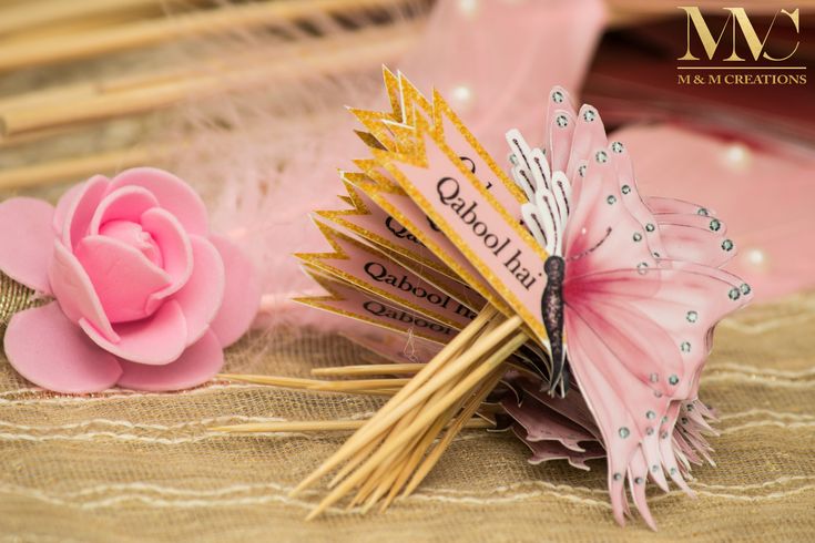 a pink flower sitting on top of a table next to some feathers and a butterfly