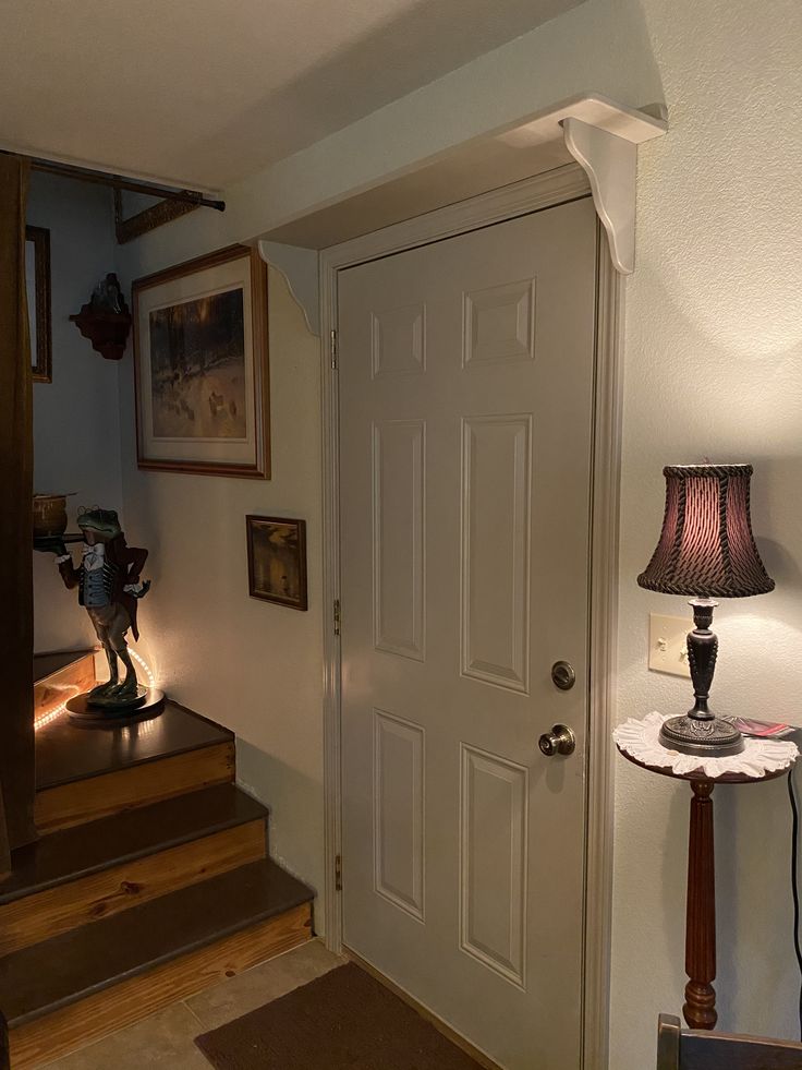 an entry way with a lamp and some pictures on the wall above it, next to a set of stairs