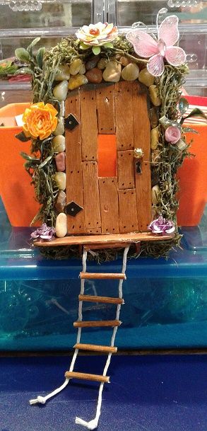 a miniature house made out of wood and rocks with flowers on the roof is sitting on a blue table