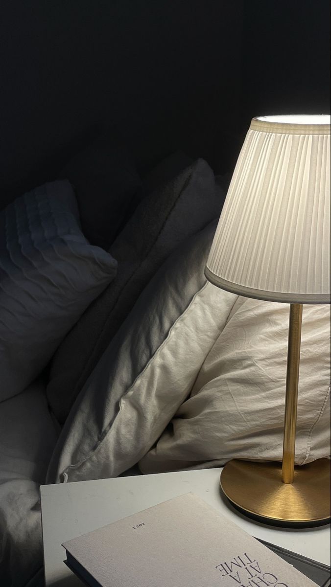 a lamp sitting on top of a table next to a book and pillow in a dark room