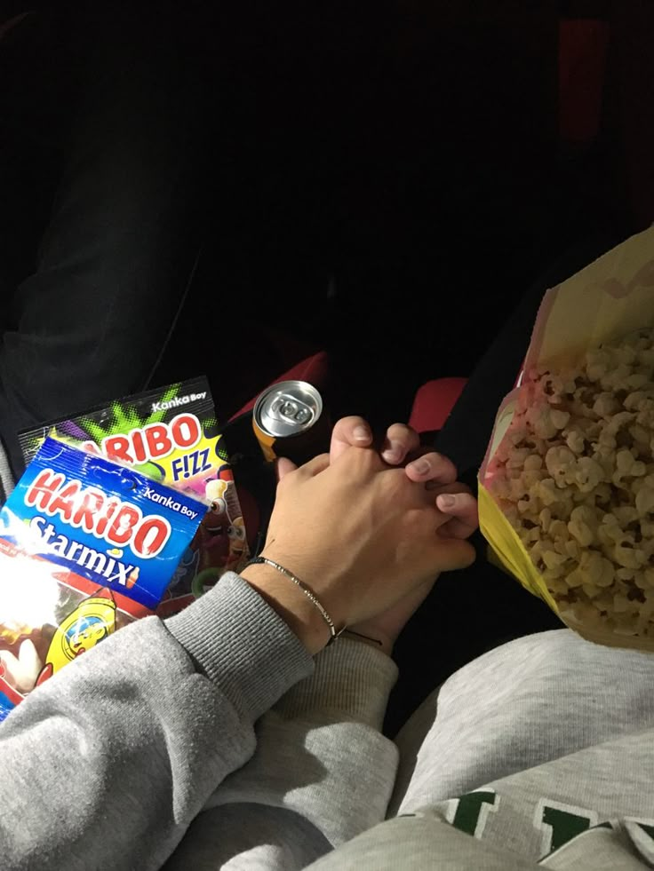 a person is eating popcorn and holding a drink in their hand while sitting on the couch