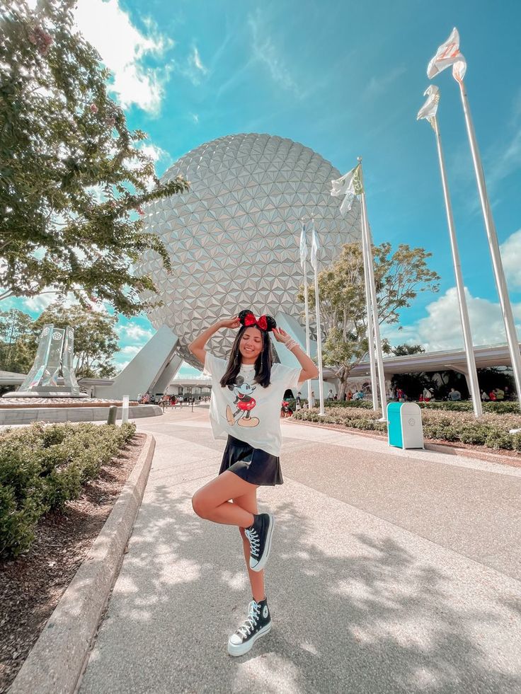 a woman poses in front of the spaceship dome at epcota disney world with her hands behind her head