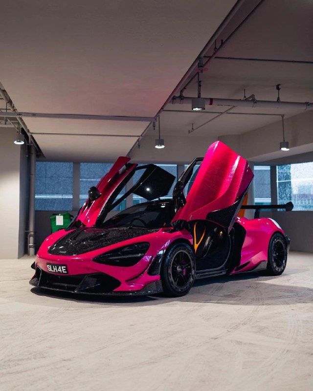 a pink and black sports car parked in a parking garage with its doors open to reveal the interior