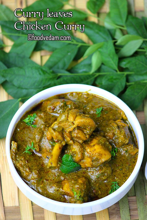 a white bowl filled with chicken curry next to green leaves