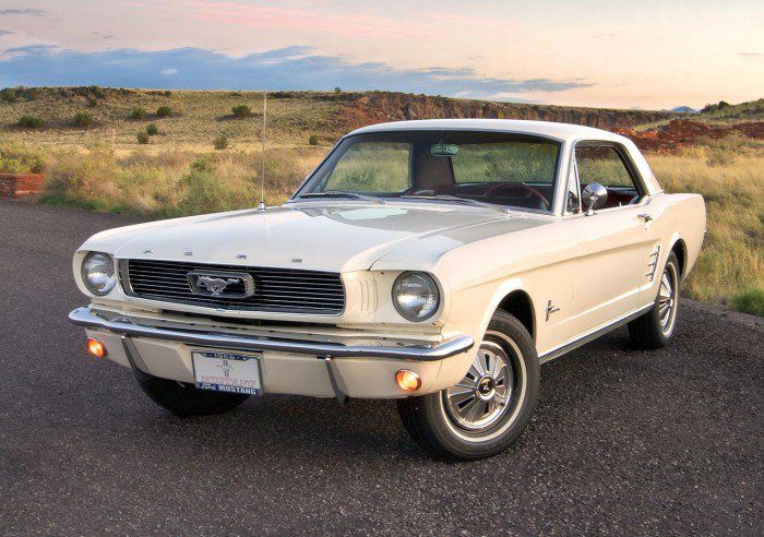 an old ford mustang is parked on the side of the road with grass in the background