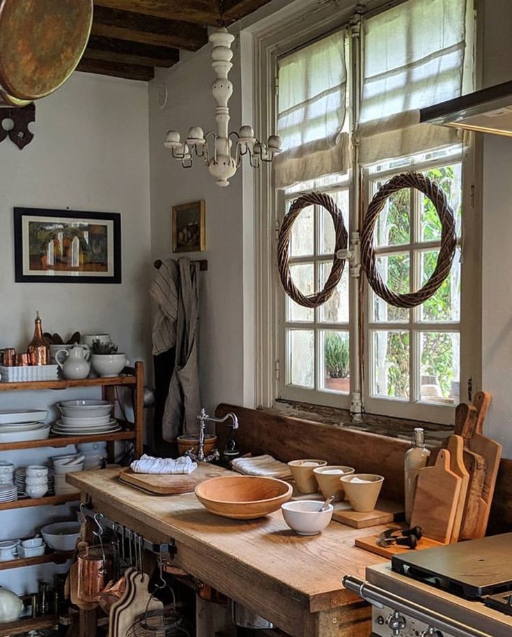 an old fashioned kitchen with lots of bowls and pans on the counter, in front of two windows