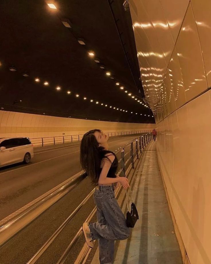 a woman leaning against a wall in an empty tunnel