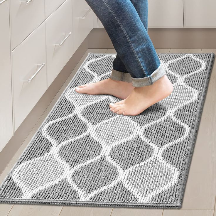 a woman standing on top of a gray rug in a kitchen next to white cabinets